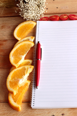 Diary book with orange and tomatoes slice on wooden background.の写真素材
