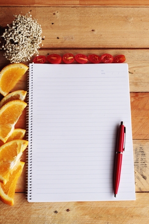 Diary book with orange and tomatoes slice on wooden background.の写真素材