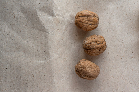 Top view, copyspace. Three inshell walnuts on old crumpled kraft paper, brown background, warm beige...
