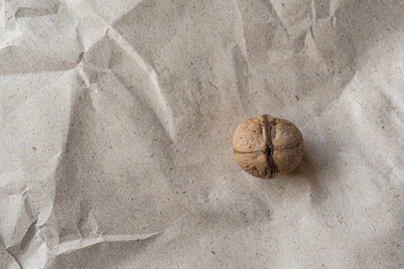 Top view. One inshell walnut on old crumpled kraft paper, brown background, warm beige pattern eco,...