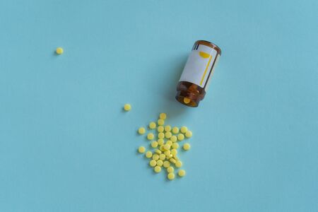 A pile of yellow round shaped pills spilled out of a glass jar on a blue background. Medical concept, virus treatment, healthcare. Medical supplies and a bottle. top viewの写真素材