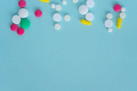 Tablets of different shapes and colors lie chaotically on top. Medical concept on a blue background, pharmacy. Empty space for text. Copy spaceの写真素材