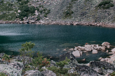 Water ripples in a green mountain lake. Man sits on a stone sticking out of the water near the shore. Summer natural landscape.の写真素材