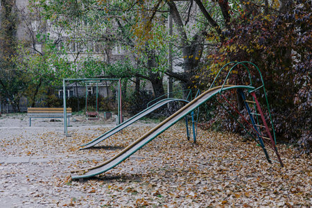 An old children's playground with metal elements in the Soviet Courtyard, strewn with fallen yellow...