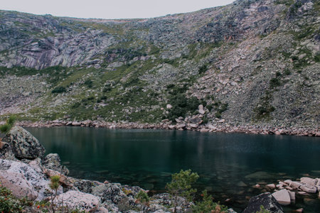 Emerald colored mountain lake surrounded by stones, rocks and trees. Secluded shore of a pond at...
