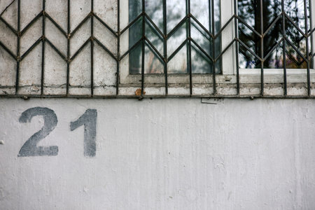 House numbering. The number 21 twenty one is painted using a stencil on a gray wall below a window with bars.の写真素材