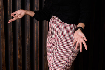 Woman in a black blouse and gingham pants in red, white and black, spreads her hands. Part of a person in the frame, without a face. Questioning pose, hand movementsの写真素材