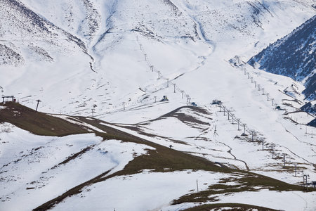 End of season, empty ski resort. Thawed patches on snowy mountain slope. Chairlifts, view from...