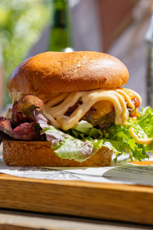 delicious gourmet burger made with a juicy patty, topped with melted cheese, fresh lettuce and generous amount of sauce creating a perfect balance of flavors. enjoyable dining atmosphere.の写真素材