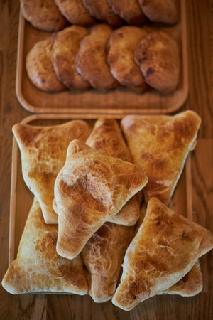 Fresh pastries on wooden plates: triangular samosas samosas with meat and sochen sochnik sweet made...