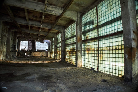 A hauntingly beautiful view of an abandoned industrial space, illuminated softly, seen through glass block walls. Abandoned Industrial Space bathed in Natural Light, uniquely atmospheric settingの写真素材