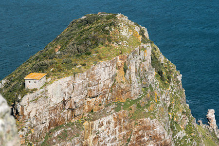 A cliff surrounded by the ocean and a house on the edge of rocky cliff.の写真素材