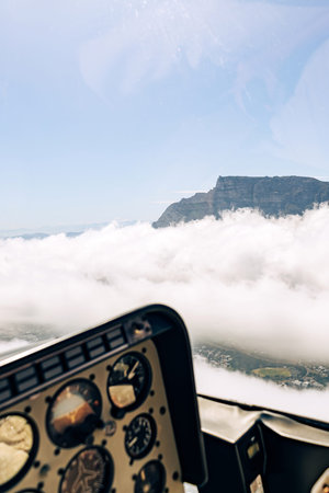 Helicopter cockpit view showing a mountain peak above clouds. Aerial transportation and scenic...