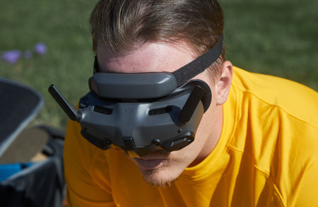 Man with brown hair wearing DJI drone FPV goggles outdoors for remote flying experience. Technology...