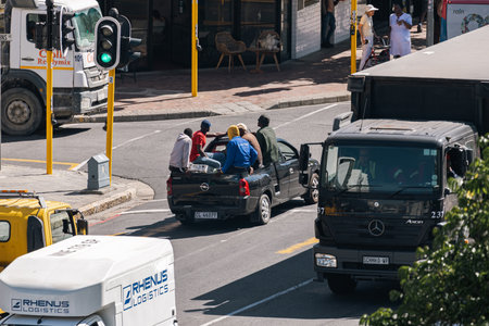 Men ride in the open back of a pickup truck along a city street, urban traffic conditions. Violations of transportation and traffic regulations. Cape Town, South Africa - 31 OCT 2023のeditorial素材