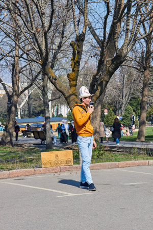 Kyrgyz man wearing Ak Kalpak headdress offering to play Alchik for money during city festival Nooruz. Traditional entertainment. Bishkek, Kyrgyzstan - 21 MAR 2023.のeditorial素材