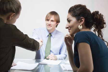 Three businesspeople in meeting. A male and female are shaking hands. Horizontally framed shot.の写真素材