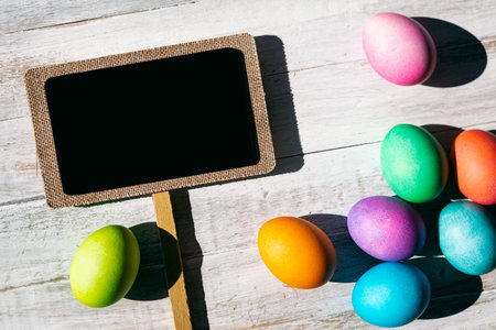 A rainbow of Easter Eggs on a white and weathered wood background.