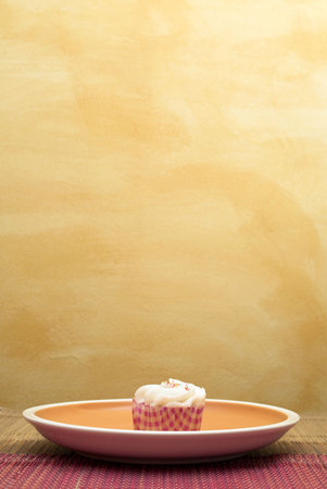one Cupcake on pink and brown table cloth in front of  wall - copy spaceの写真素材