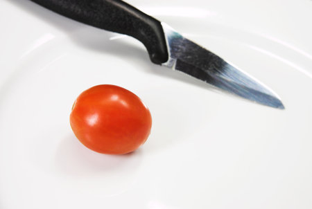 A knife and a cherry tomato on a white plate.の写真素材