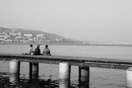 Three kids fishing from the pier on Ile Sante-Marguerite  Cannes in Background, France - Black and Whiteの写真素材