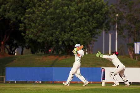 Cricketers playing in the late afternoon, Batsman hitting ball, wicketkeeper trying to catchの写真素材