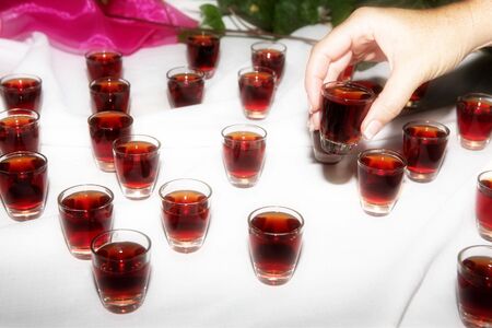 Woman taking sherry from a table at a wedding celebration. More little glasses of alcohol is standing on a white table clothの写真素材