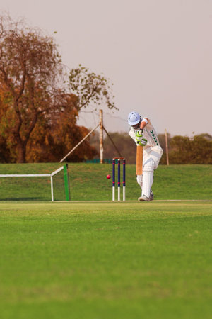 Cricketers playing in the late afternoon, Batsman hitting ball on green cricket pitch - Overcast...