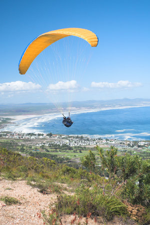 Paraglider launching from the ridge with an orange canopy and the sun from behind. The paraglider is standing out against the blue sky and the shot is taken right after takeoff. The paraglider and pilot is both sharpの写真素材