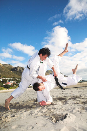 Young adult men with black belt practicing fighting on the beach on a sunny day  movement on extremities の写真素材