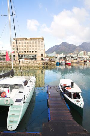 Two tourist boats in the Cape Town waterfront harbor with three boats reflecting in the water in the background and part of the city skyline visibleの写真素材