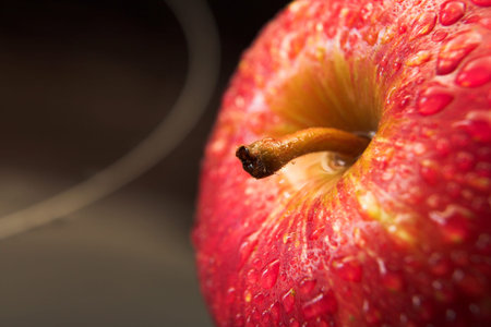 Close up view of a shiny red apple on a reflective black glass working surface with water drops on...