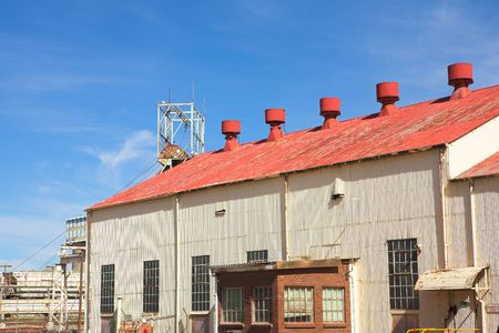 Corrugated iron building with red roof on mine premises with shaft winch in the background. Blue sky and sunny dayの写真素材