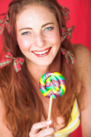 Young female adult fashion model with natural red hair and freckles in a yellow bikini with a big multi-colored lollipop (textured red faux leather background) - Very Shallow Depth of Fieldの写真素材