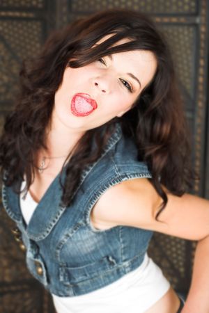 Young adult brunette woman with a white top and long brown curly hair and brown eyes looking at the camera and sticking her tongue out  Shallow DOFの写真素材