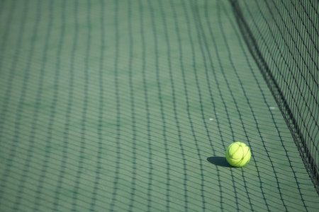 Yellow tennis ball on a green tennis court right next to the net