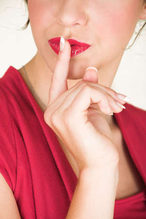 Young adult brunette businesswoman with her finger in front of her lips and wearing a red dress. She is Caucasian and wears bright red lipstick. White background, not Isolated - Shallow Depth of Fieldの写真素材