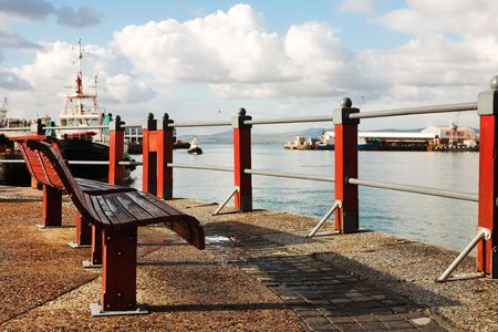 Two red seats at the Cape Town Waterfront harbour in South Africa, with boats in the background on a cloudy day.の写真素材