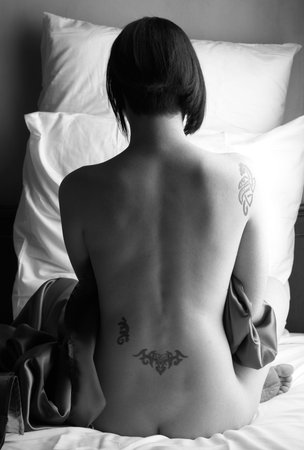 Sensual naked young Black haired adult Caucasian woman, wrapped in a charcoal colored satin, silk sheet on a bed in her bedroom. High contrast lighting.\rの写真素材