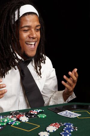Young African man with dreadlocks playing cards, chips and players gambling around a green felt poker table. Shallow Depth of fieldのeditorial素材