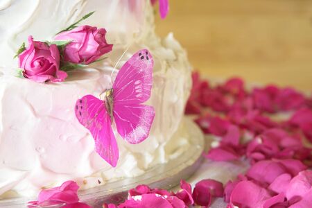 Vanilla wedding cake with white icing, rose petals and pink butterfliesの写真素材