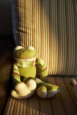 Green handmade knitted toy frog sitting in the last sunbeam of sunset on a brown corduroy and leather couch. Very shallow Depth of Field, natural light.の写真素材