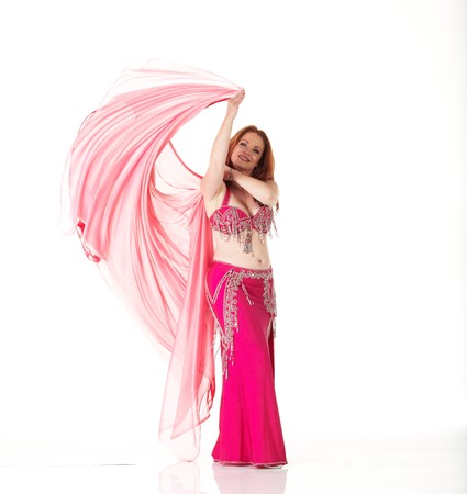 Lithe adult caucasian belly dancer with red hair and pink belly dancing outfit performing a dance with veils on a white background. Not Isolatedの写真素材