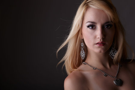 Young adult nude caucasian woman with blonde hair and prominent jewelry on a neutral grey background. Implied Nudity の写真素材