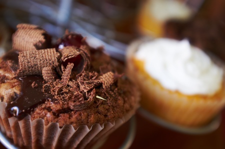 Chocolate and cream filled cupcakes with glazed cherries and chocolate shavings on a display stand  Shallow Depth of field with focus on the chocolate cupcakeの写真素材