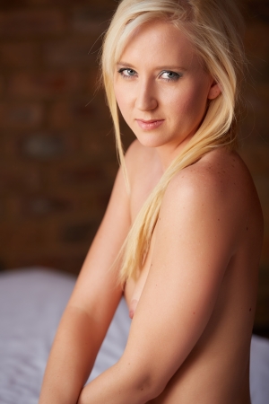 Beautiful and very sexy young adult caucasian woman in Black lingerie with blonde hair and blue eyes, in a bedroom setting with typical boudoir posesの写真素材