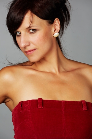 Beautiful and mature adult caucasian woman with red lips, dark hair and brown eyes wearing a open shoulder red top on a neutral grey and white background.の写真素材