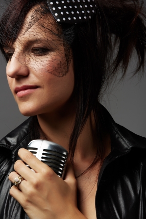 Beautiful and mature adult caucasian woman with red lips, dark hair and brown eyes wearing a black leather jacket and holding a microphoneの写真素材