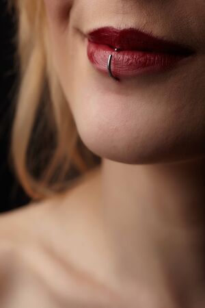Close up portrait of the pierced red lips of a beautiful young adult caucasian woman in a black gownの写真素材