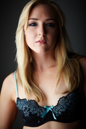 Beautiful young adult caucasian woman with blue eyes and shoulder length blonde hair wearing a sexy blue and black bra  Against a neutral background の写真素材